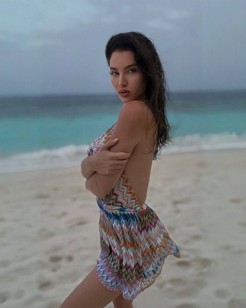 Woman in a colorful zigzag one-piece swimsuit looks over her shoulder on a sandy beach.
