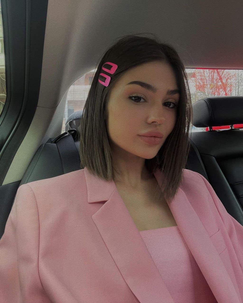 Rafaella sits in a car back seat wearing a pink blazer and ribbed top, with a brown bob and pink hair clips.
